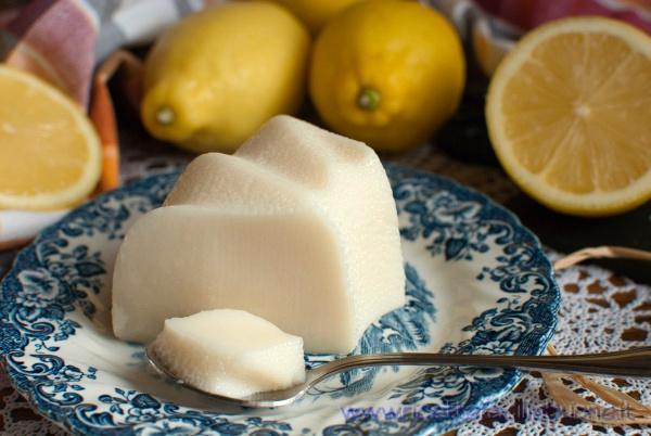 Budino al limone con amido di mais pronto da gustare su un piatto da dolce decorato e limoni sfusi sullo sfondo